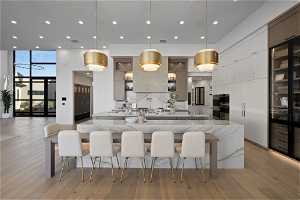 Kitchen with light hardwood / wood-style flooring, a large island, tasteful backsplash, white cabinets, and pendant lighting