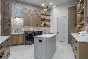 Laundry area featuring sink, washer and dryer, light tile floors, and an inviting chandelier