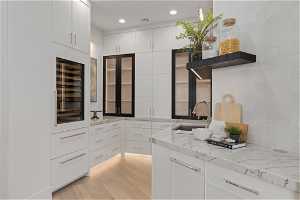 Kitchen featuring wine cooler, white cabinets, light hardwood / wood-style flooring, sink, and light stone counters