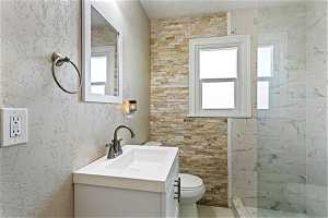 Bathroom featuring a healthy amount of sunlight, toilet, vanity, and stone detail.