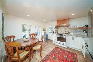 Kitchen with range with two ovens, light laminate flooring, white cabinets, and backsplash
