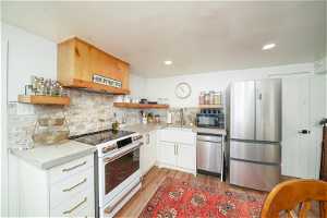 Kitchen with light laminate flooring, stainless steel appliances, tasteful backsplash, white cabinets, and sink