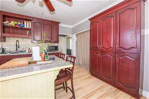 Kitchen with a kitchen bar, light hardwood / wood-style flooring, ceiling fan, crown molding, and tasteful backsplash