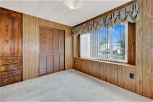 Unfurnished bedroom with a closet, wood walls, and carpet