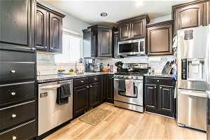 Kitchen featuring appliances with stainless steel finishes, light hardwood / wood-style floors, tasteful backsplash, dark stone countertops, and sink