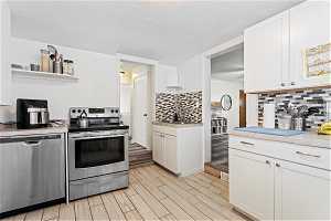 Kitchen featuring light wood-type flooring, backsplash, white cabinetry, and stainless steel appliances