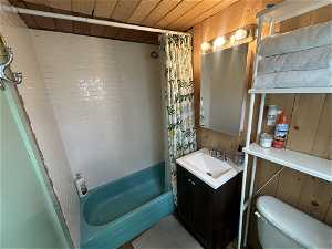 Full bathroom featuring wood walls, shower / bath combination with curtain, toilet, vanity, and wooden ceiling