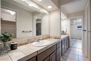 Bathroom featuring dual sinks, vanity with extensive cabinet space, and tile floors