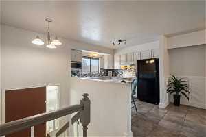 Kitchen with dark tile flooring, backsplash, white electric range, stainless steel microwave, and black refrigerator