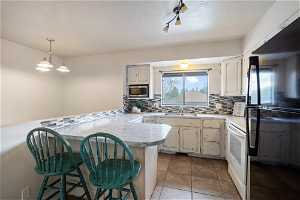 Kitchen with kitchen peninsula, black fridge, backsplash, stainless steel microwave, and light tile floors