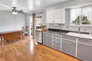 Kitchen with ceiling fan, white cabinets, sink, light wood-type flooring, and stainless steel dishwasher