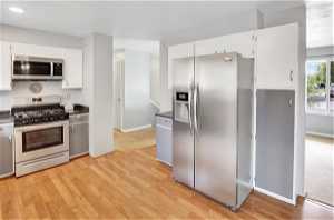 Kitchen with light hardwood / wood-style flooring, stainless steel appliances, and white cabinetry