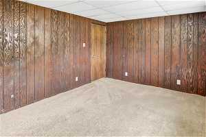 Carpeted empty room featuring wood walls and a paneled ceiling