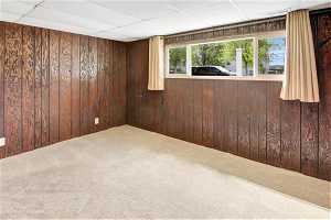 Carpeted spare room with wood walls and a paneled ceiling