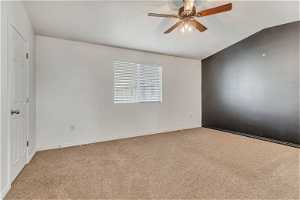 Spare room with ceiling fan, carpet floors, and vaulted ceiling