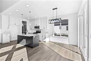 Kitchen featuring white cabinets, tasteful backsplash, decorative light fixtures, stainless steel appliances, and a center island with sink