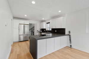 Kitchen featuring built in fridge, kitchen peninsula, light wood-type flooring, and white cabinetry