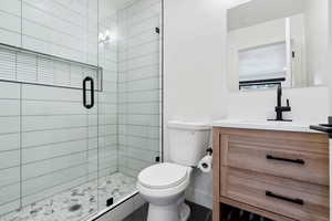 Bathroom featuring a shower with door, vanity, and toilet