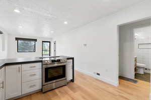 Kitchen with stainless steel range with electric stovetop, tile walls, light hardwood / wood-style flooring, and a textured ceiling