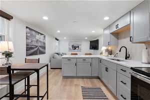 Kitchen with kitchen peninsula, gray cabinetry, light hardwood / wood-style flooring, tasteful backsplash, and sink