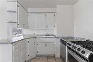 Kitchen featuring kitchen peninsula, stainless steel appliances, light tile flooring, white cabinetry, and sink