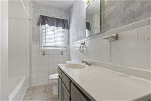 Full bathroom featuring tile flooring, tile walls, toilet, and vanity with extensive cabinet space