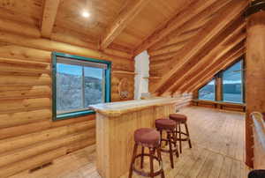 Bar with light hardwood / wood-style flooring, tile counters, vaulted ceiling with beams, wooden ceiling, and log walls