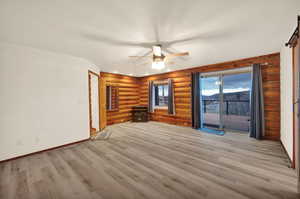 Unfurnished room featuring ceiling fan, light wood-type flooring, and rustic walls