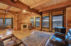 Living room with beamed ceiling, a wealth of natural light, log walls, and light wood-type flooring