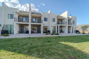 Back of property with a balcony, a patio, and a lawn