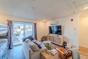 Living room with a wall unit AC, a textured ceiling, and hardwood / wood-style floors