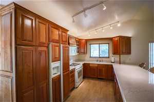 Kitchen featuring sink, white appliances, rail lighting, vaulted ceiling, and light hardwood / wood-style flooring