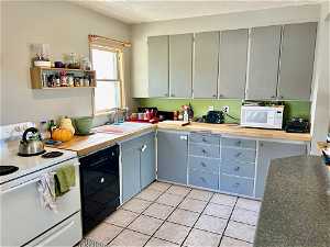 Kitchen with sink, white appliances, light tile flooring, and built in desk