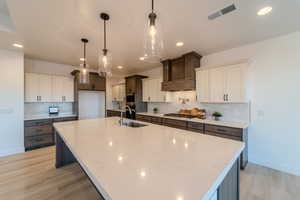 Kitchen with custom range hood, decorative backsplash, and white cabinetry