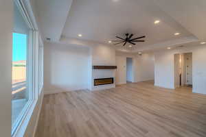 Unfurnished living room featuring ceiling fan, a raised ceiling, and light hardwood / wood-style flooring