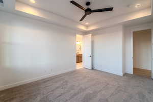 Unfurnished bedroom with ceiling fan, connected bathroom, light carpet, and a tray ceiling