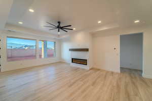 Unfurnished living room with ceiling fan, light hardwood / wood-style floors, and a tray ceiling