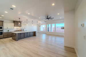 Kitchen featuring light hardwood / wood-style flooring, decorative light fixtures, oven, an island with sink, and built in microwave