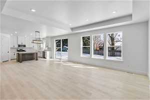 Unfurnished living room with sink, light hardwood / wood-style floors, and a tray ceiling