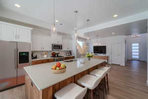 Kitchen with white cabinets, light hardwood / wood-style floors, appliances with stainless steel finishes, decorative backsplash, and a spacious island