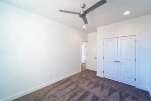 Unfurnished bedroom with a closet, ceiling fan, and dark carpet