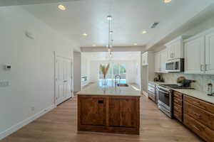 Kitchen with white cabinetry, stainless steel appliances, sink, light hardwood / wood-style flooring, and a kitchen island with sink