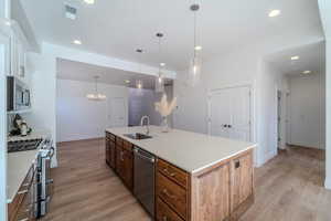 Kitchen with stainless steel appliances, sink, pendant lighting, light hardwood / wood-style floors, and a kitchen island with sink