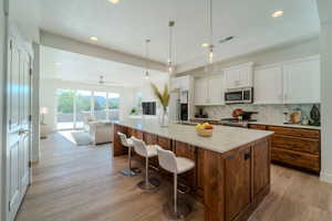 Kitchen featuring stainless steel appliances, decorative backsplash, white cabinets, a center island, and light hardwood / wood-style flooring