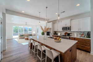 Kitchen with white cabinets, stainless steel appliances, light hardwood / wood-style flooring, and an island with sink