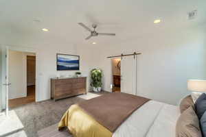 Carpeted bedroom featuring ensuite bath, ceiling fan, and a barn door