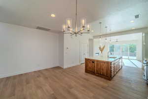 Kitchen featuring a textured ceiling, an island with sink, hardwood / wood-style flooring, decorative light fixtures, and sink