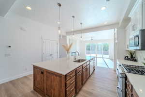 Kitchen with decorative light fixtures, an island with sink, sink, light hardwood / wood-style floors, and range with gas cooktop