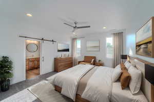 Carpeted bedroom with ceiling fan, connected bathroom, and a barn door