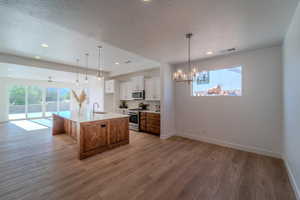 Kitchen with white cabinetry, light wood-type flooring, a center island with sink, range with gas stovetop, and sink